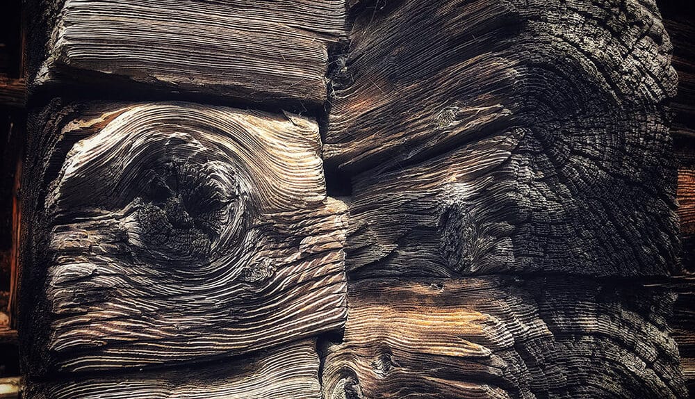 Der Blockbau – Tradition in Holz Dieses Detail zeigt die beeindruckende Konstruktion eines alten Walliser Hauses: massive Holzbalken, die sich an den Ecken kreuzen, mit sichtbaren Jahresringen und Spuren der Zeit. Der sogenannte Blockbau – im Wallis auch Strickbau genannt – gehört neben dem Ständer- und Fachwerkbau zu den klassischen Holzbautechniken. Dabei werden die Stämme waagrecht aufeinandergeschichtet, an den Enden eingeschnitten und über Kreuz miteinander verbunden. Die so entstehenden Eckverbindungen heißen „Blockvorstösse“ oder im Dialekt „Gwätti“. Archäologische Funde belegen, dass diese Bauweise im Wallis schon seit keltischer Zeit, also seit über zweitausend Jahren, genutzt wird. Solide, dauerhaft und zugleich ästhetisch – der Blockbau ist ein eindrückliches Zeugnis traditioneller Handwerkskunst, das bis heute in den alten Häusern der Region sichtbar bleibt. Bildunterschrift: Ein „Gwätti“ – die traditionelle Eckverbindung am Blockbau eines Walliser Hauses